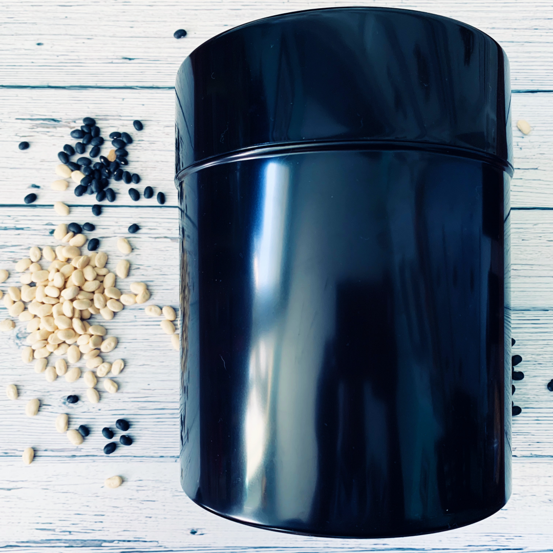 Extra-large black seed storage vault container with vacuum-seal lid and scattered seeds on white wooden surface